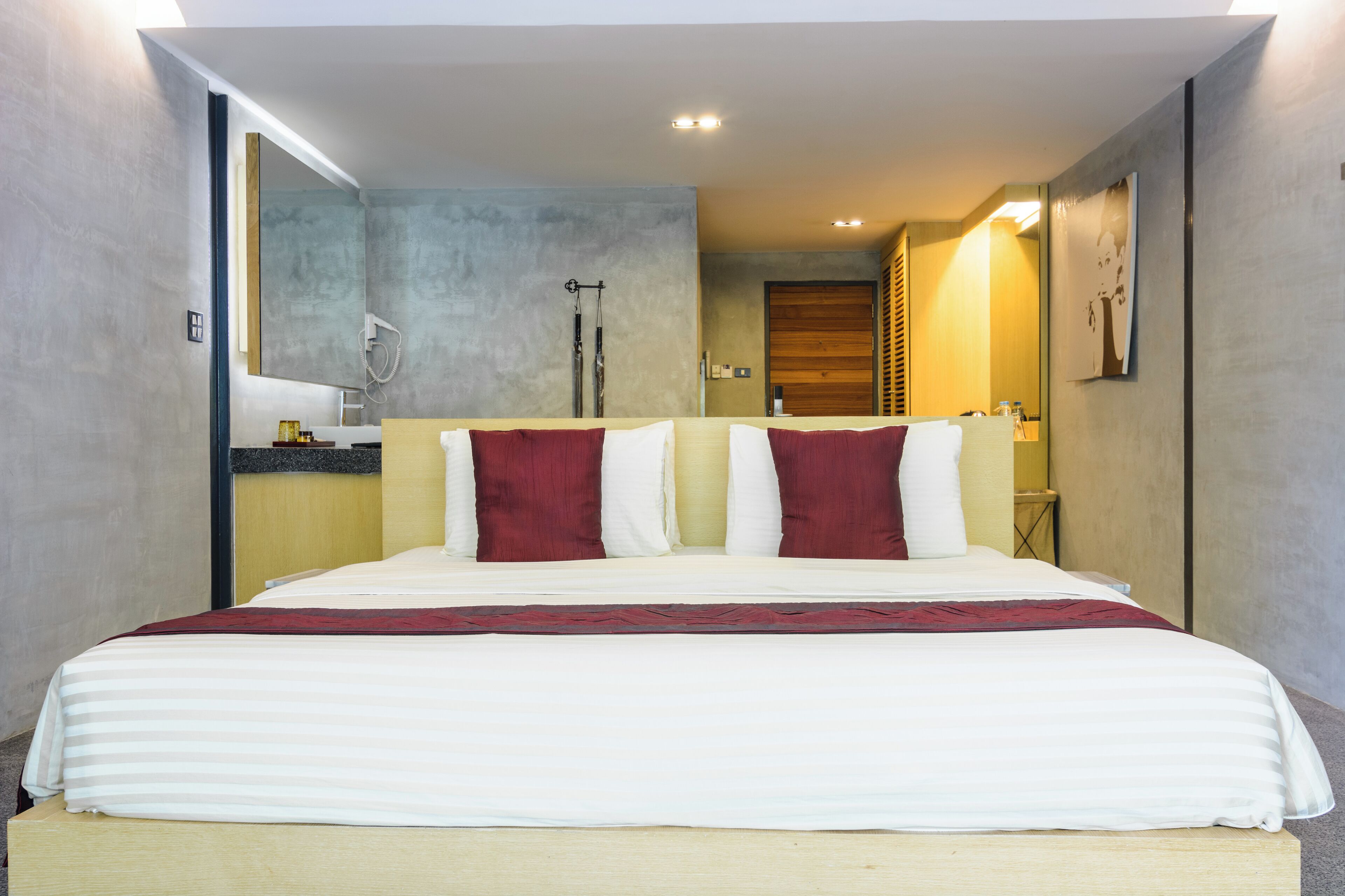 Una habitación de hotel moderna con una cama grande, cabecera de madera y un baño a la vista.