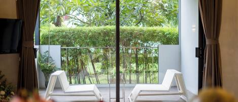 A room with a balcony, two white lounge chairs, a small table, and a TV on the wall.