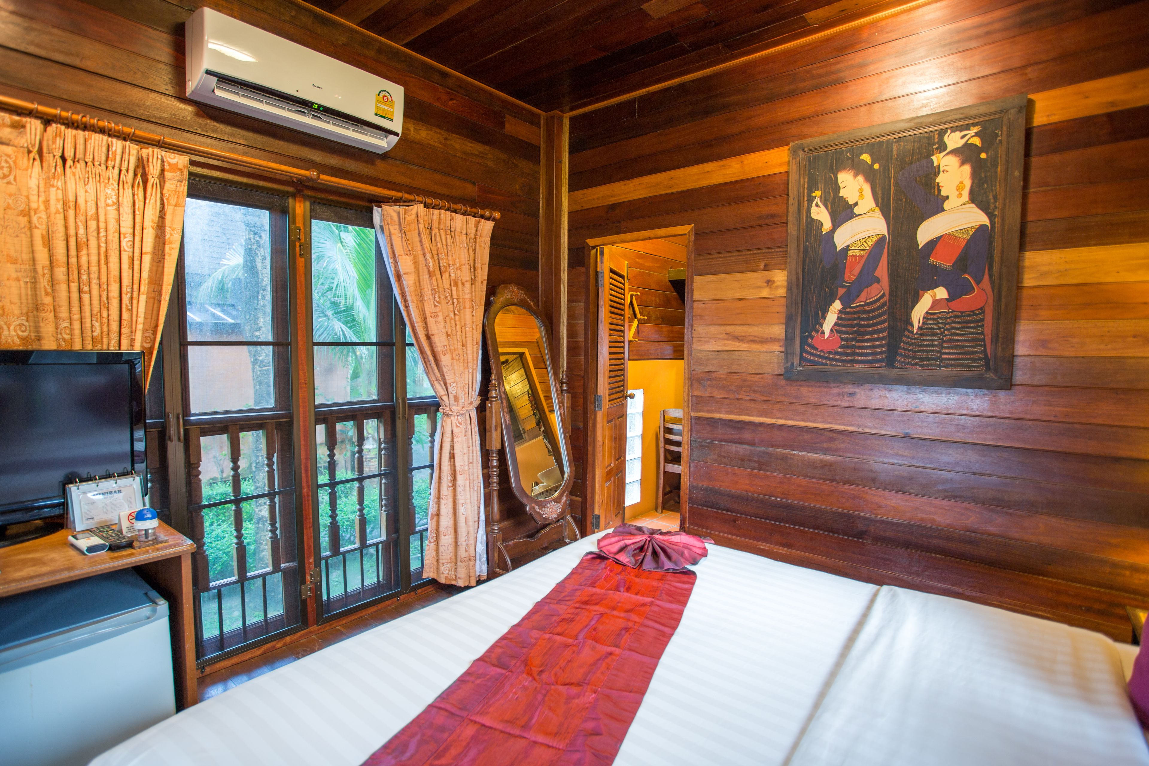 Una habitación de madera con cama, televisor, espejo y ventana con cortinas.