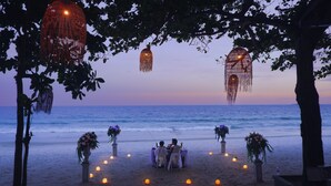 Una ceremonia de boda al aire libre con un entorno de playa, mostrando una pareja sentada en una mesa rodeada de velas y arreglos florales.