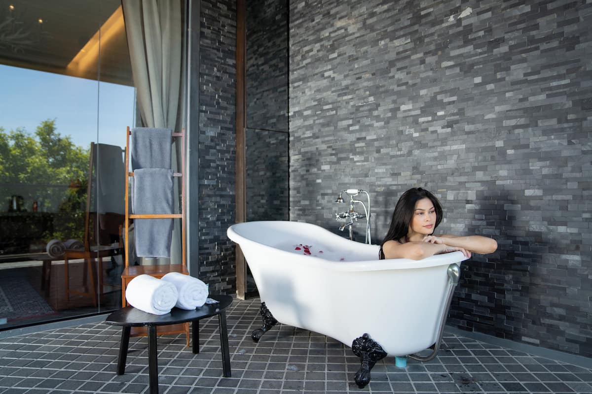 A modern bathroom with a freestanding bathtub, a glass shower enclosure, and a wooden chair with towels.
