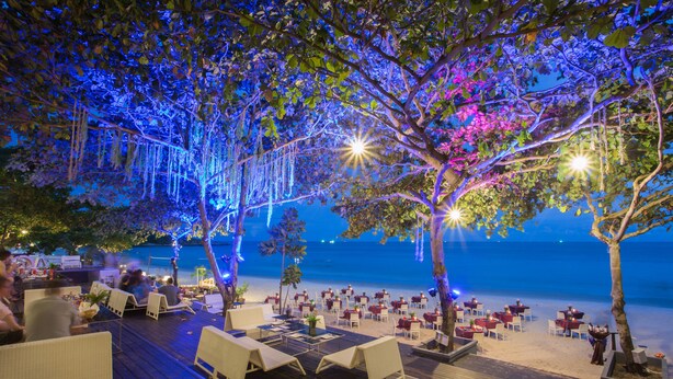 Un área de comedor al aire libre con mesas y sillas, con vistas a la playa.