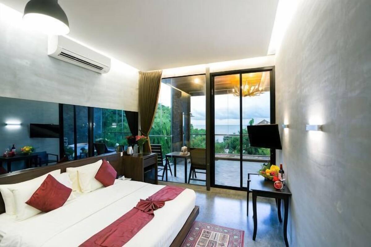 A hotel room with a bed, a desk, a chair, a TV, and a balcony with a view.