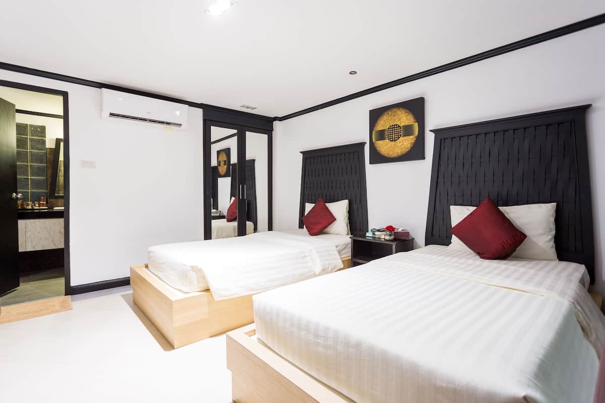 A hotel room with two beds, a mirror, a wall-mounted air conditioner, and a small table with a red pillow.