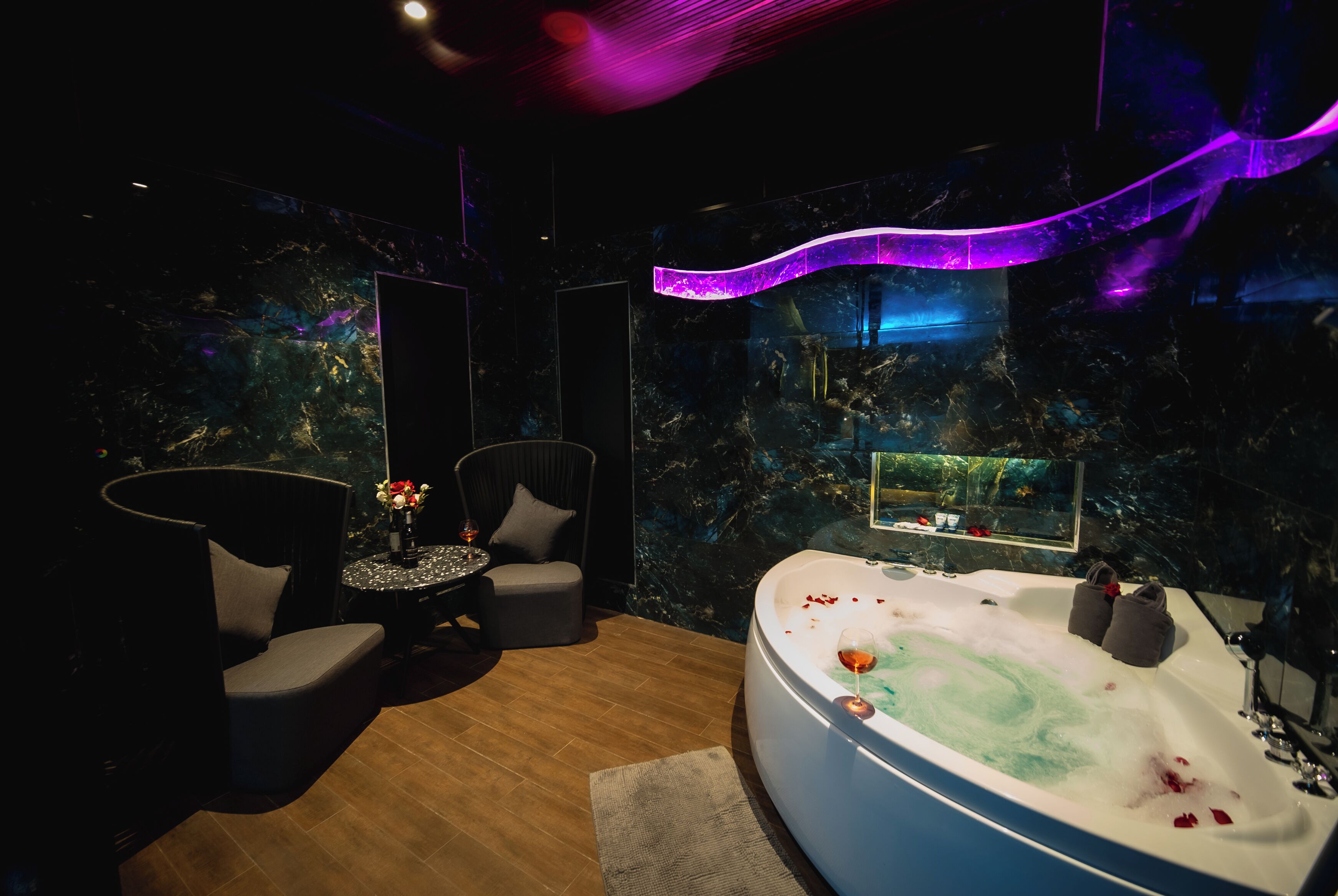 A modern bathroom with a large bathtub, a mirror, and a seating area with a small table and chairs.