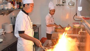 Un chef cuisinant devant une grande flamme sur une cuisinière dans une cuisine.