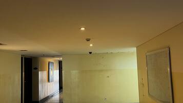 Corredor com luminária no teto, uma porta e tela fixada na parede.