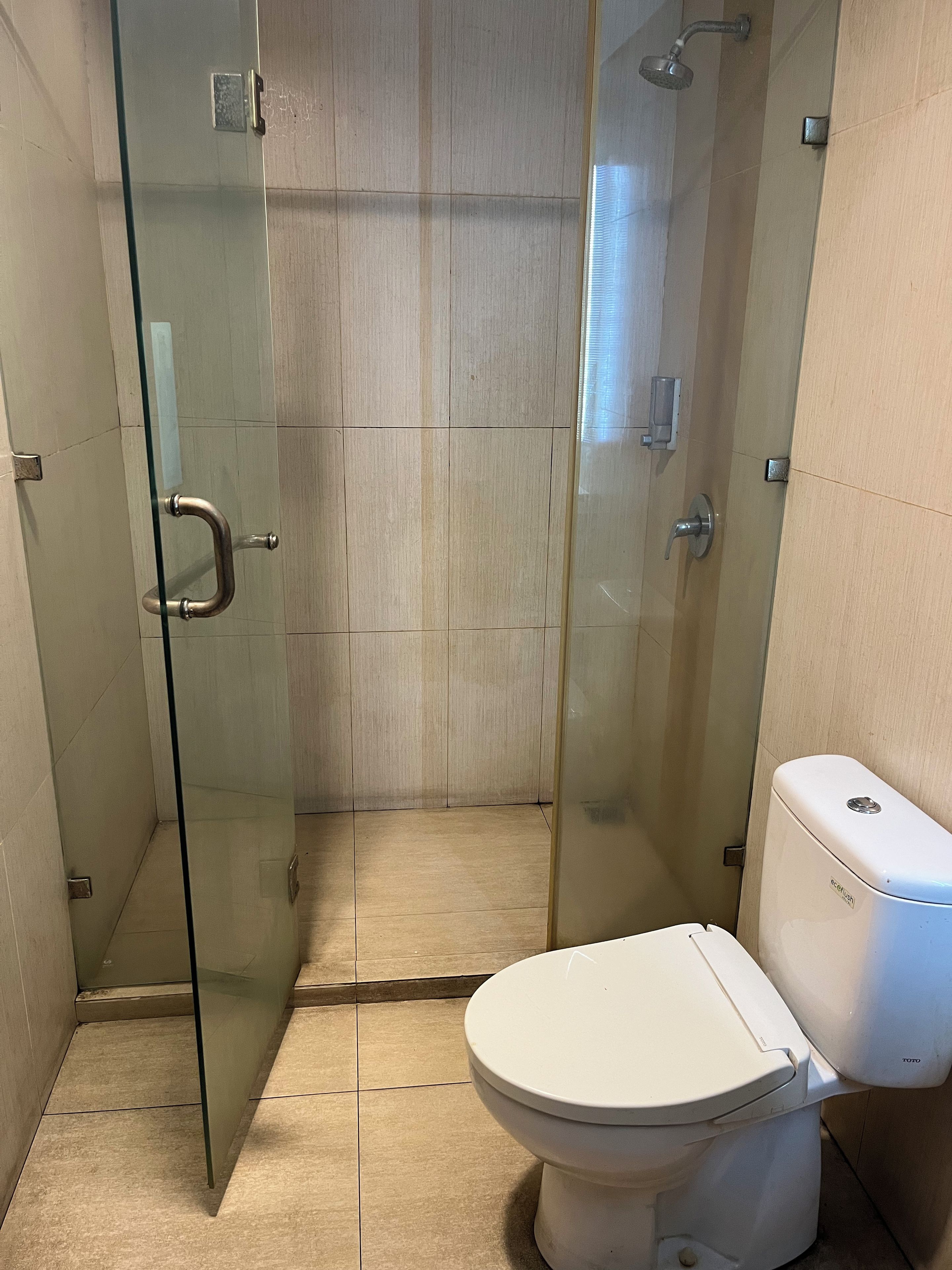 A bathroom with a glass-enclosed shower, a toilet, and tiled walls.