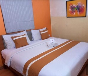Una habitación de hotel con una cama, almohadas, una colcha y un cuadro en la pared.