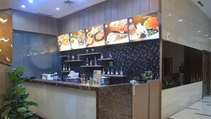 Un espace d’accueil avec un comptoir en marbre, un mur recouvert de carreaux représentant des images de nourriture et une plante sur le côté gauche.
