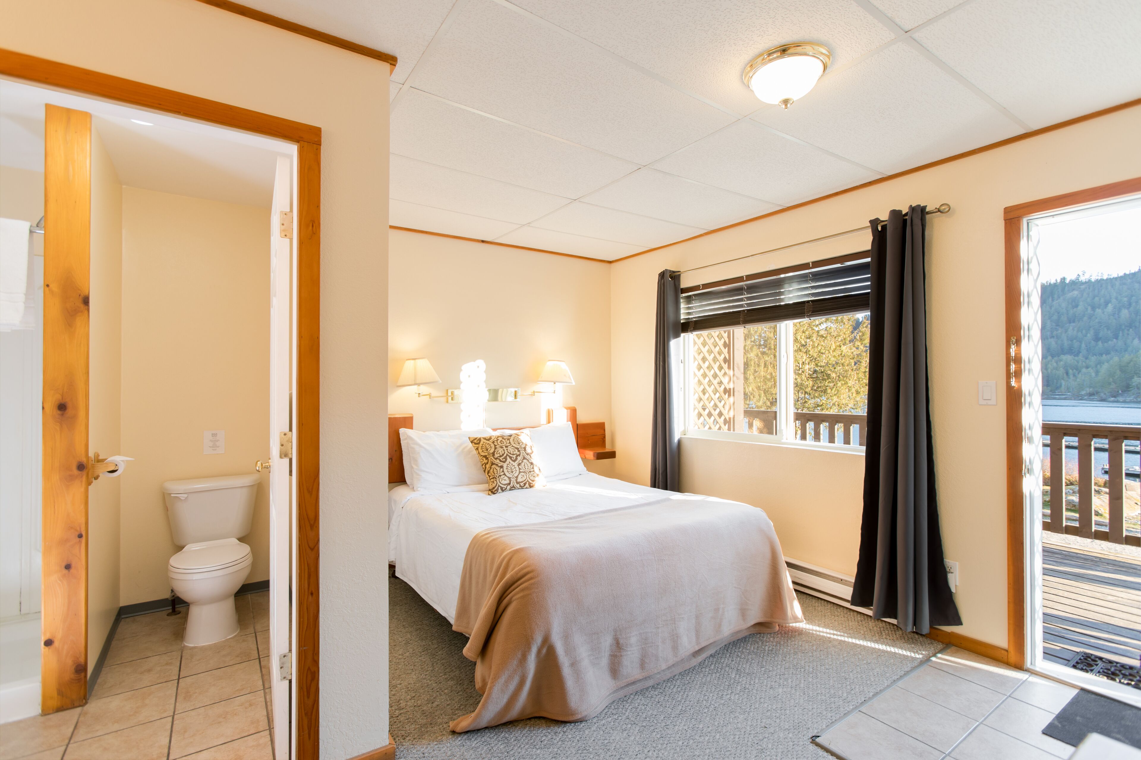 A bedroom with a bed, bedside lamps, a window with a view, and a door leading to a bathroom.