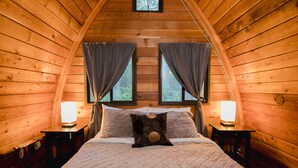 Een knus slaapkamer in een blokhut met een groot bed, twee bedlampen en gordijnen voor de ramen.
