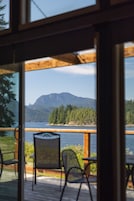 Vista desde una terraza de madera con sillas y una mesa, con vista a un lago y montañas.