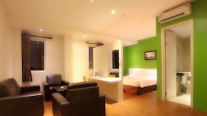 Habitación de hotel con cama, escritorio, dos sillas, ventana con cortinas y un equipo de aire acondicionado.