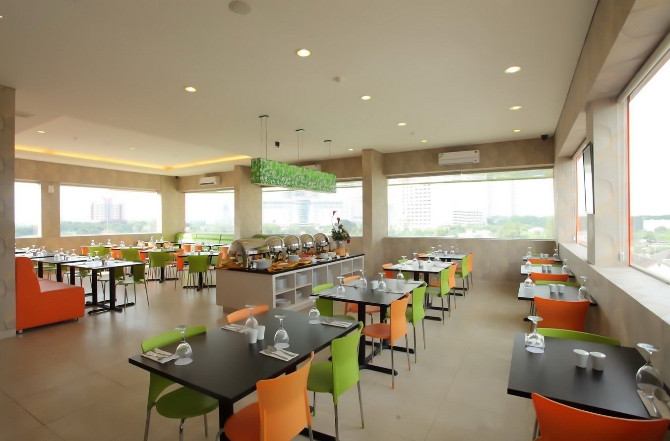 A modern dining area with multiple tables and chairs, large windows offering a city view, and a central counter with food items.