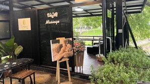A massage parlor with a sign for 'Wellness The Place' and a 'Massage' sign. There is a wooden bench and a table with a flower arrangement. - The Piano Resort (Pak Chong)
