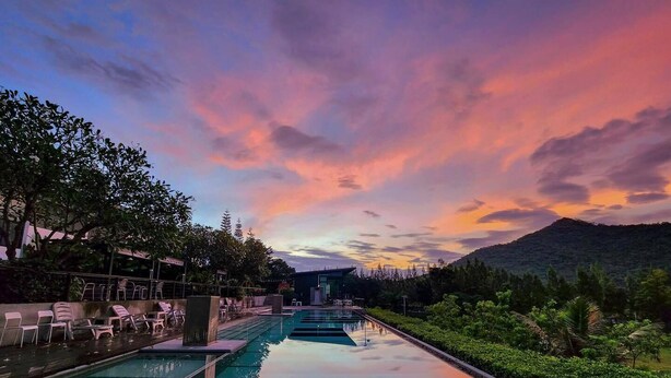 A swimming pool with a view of a mountain and trees at sunset. - The Piano Resort (Pak Chong)