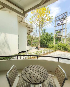 Un balcón con una mesa redonda de madera y dos sillas, con vista a un jardín con árboles y un poste de electricidad.