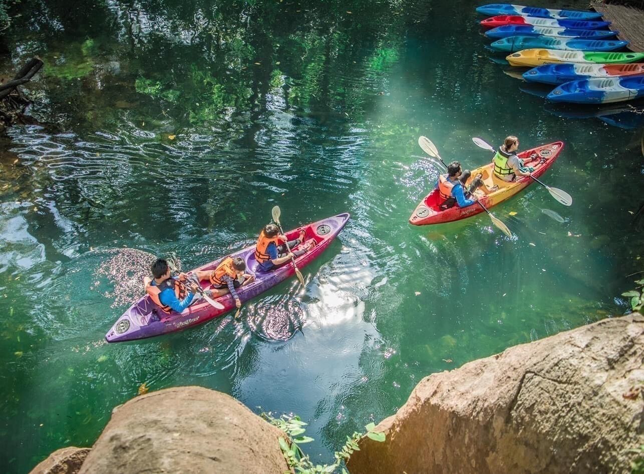 Dos kayaks en un río tranquilo con agua cristalina, rodeado de rocas y vegetación.