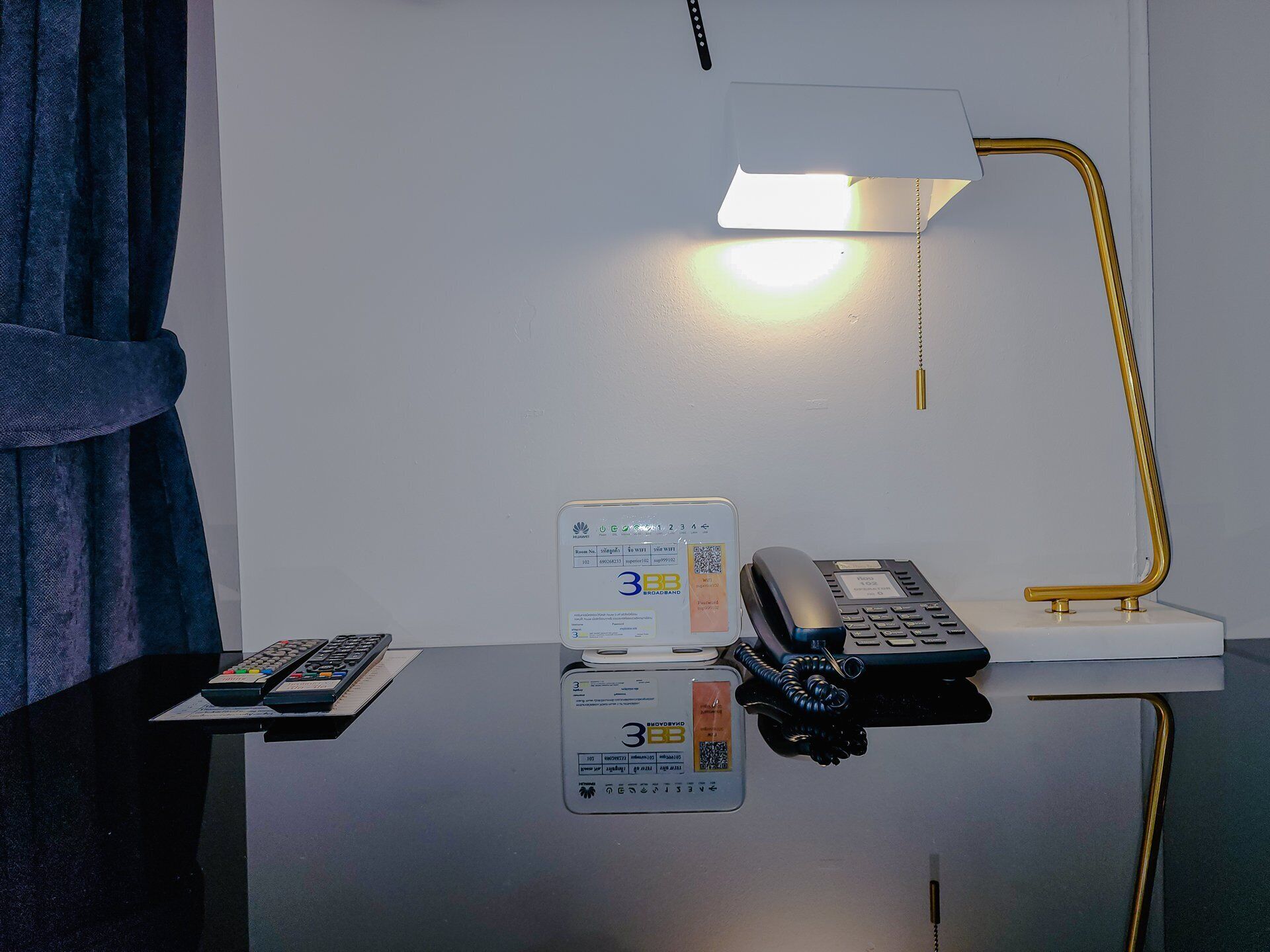 Ein Hotelzimmer mit einem Schreibtisch, der eine Schreibtischlampe, ein Telefon, eine Fernbedienung und eine Karte beherbergt.