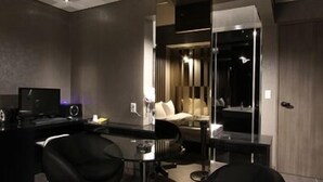 A modern, dimly lit room with a dark color scheme, featuring a bar area with stools, a sofa, and a large mirror. - Valentine Hotel (Goyang)