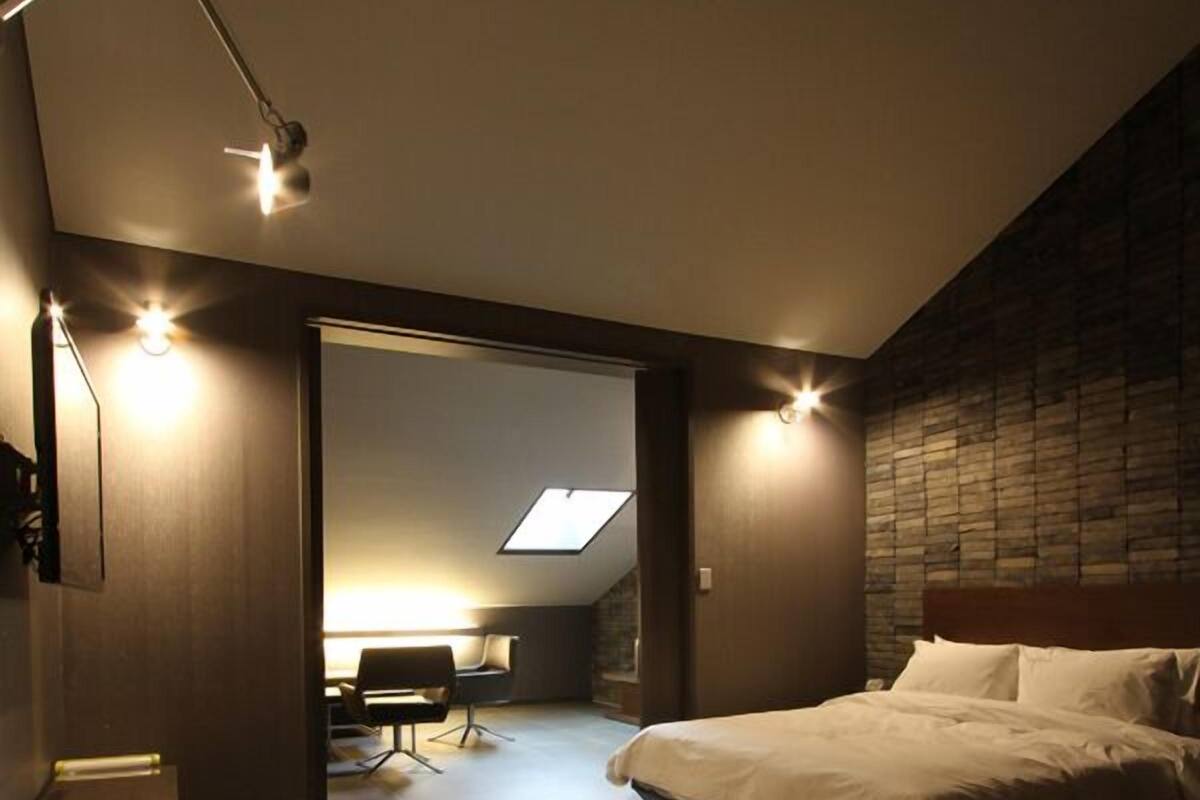 A modern bedroom with a large bed, a desk, and a skylight.