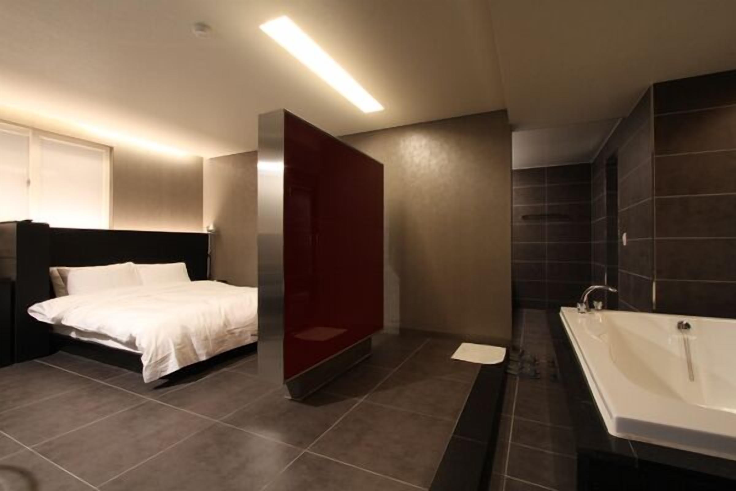 A modern bathroom with a large bathtub, a separate shower area, and a bed with a white comforter.
