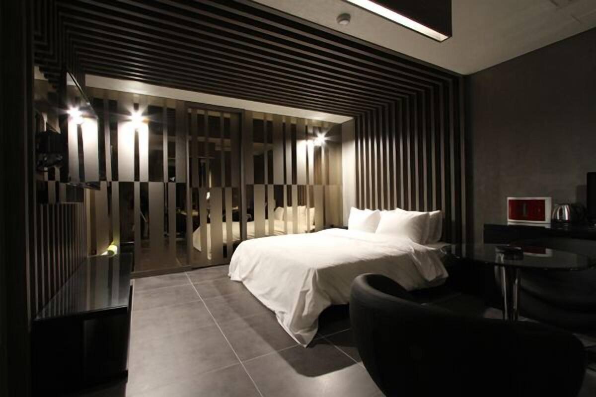 A modern hotel room with a large bed, a desk, and a chair.