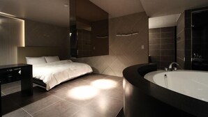 A modern bedroom with a large bed, a vanity with a mirror, and a bathtub. - Valentine Hotel (Goyang)