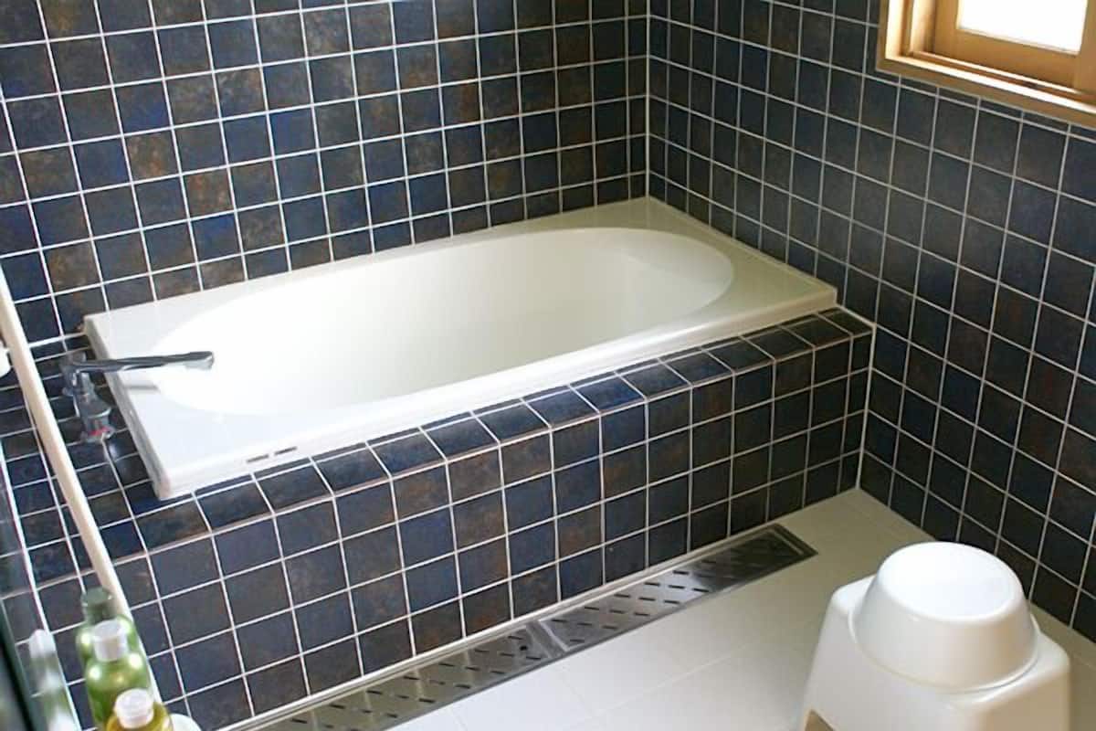 A bathroom with a white bathtub, dark blue tiles, a white toilet, and a shower area.