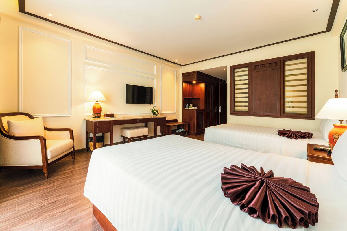 Ein Hotelzimmer mit einem großen Bett, einem Schreibtisch, einem Sessel, einem Fernseher und einem Kleiderschrank.