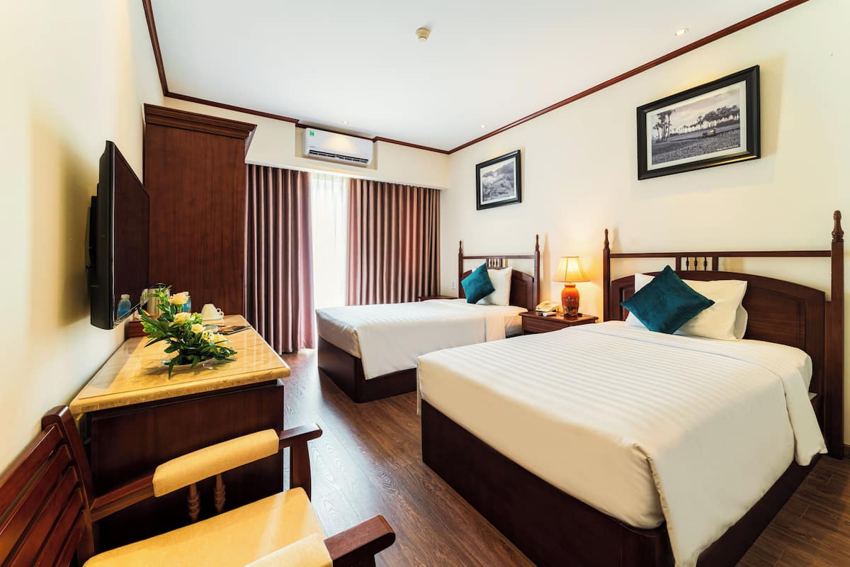 Ein Hotelzimmer mit zwei Betten, einem Schreibtisch mit Stuhl, einem Fernseher und einem Fenster mit Vorhängen.