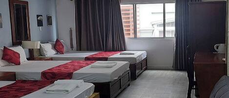 A hotel room with three beds, a sofa, a desk, and a window with curtains.