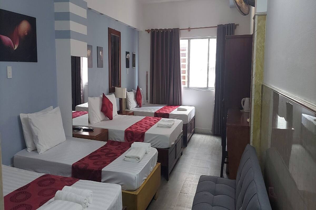 A hotel room with three beds, a desk, a chair, and a large window with curtains.