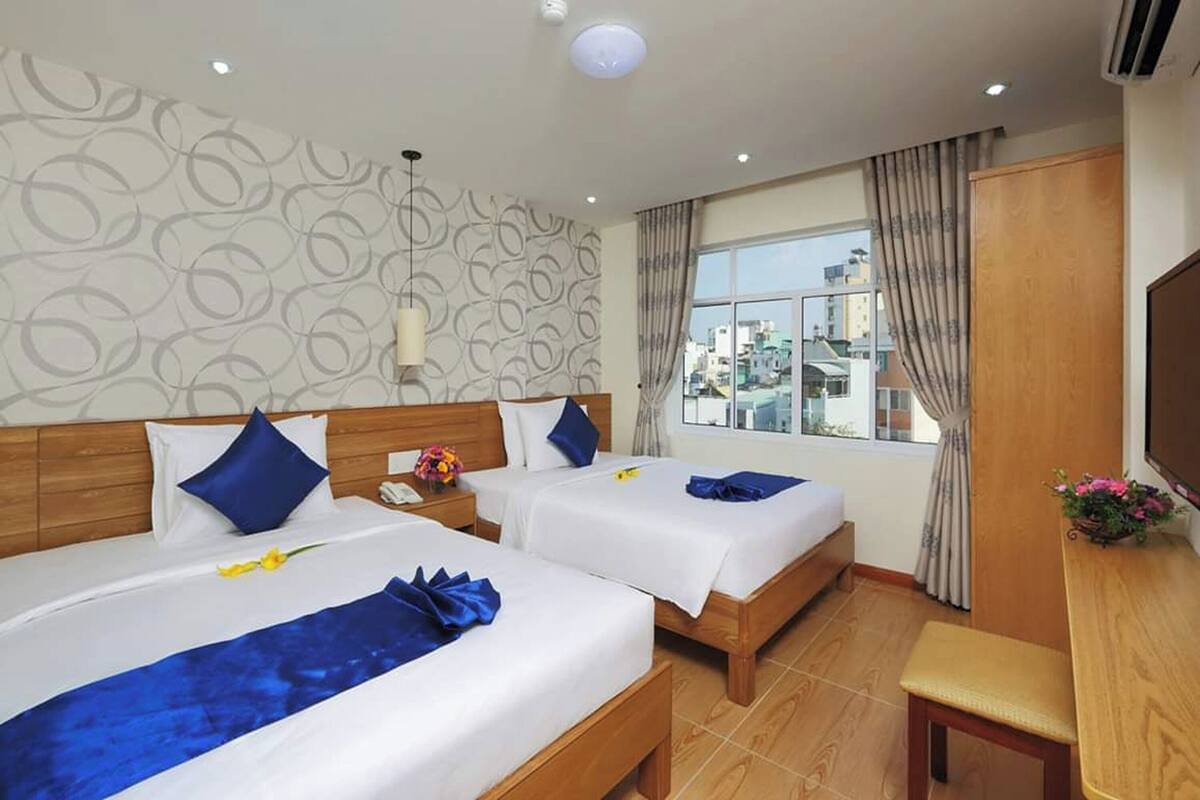 A hotel room with two beds, a wooden headboard, a small table, a TV, and a window with curtains.