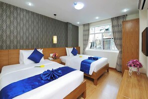 A hotel room with two beds, a wooden headboard, a window with curtains, a wall-mounted TV, and a small table with a flower arrangement. - Ailen Hotel (Ho Chi Minh City)