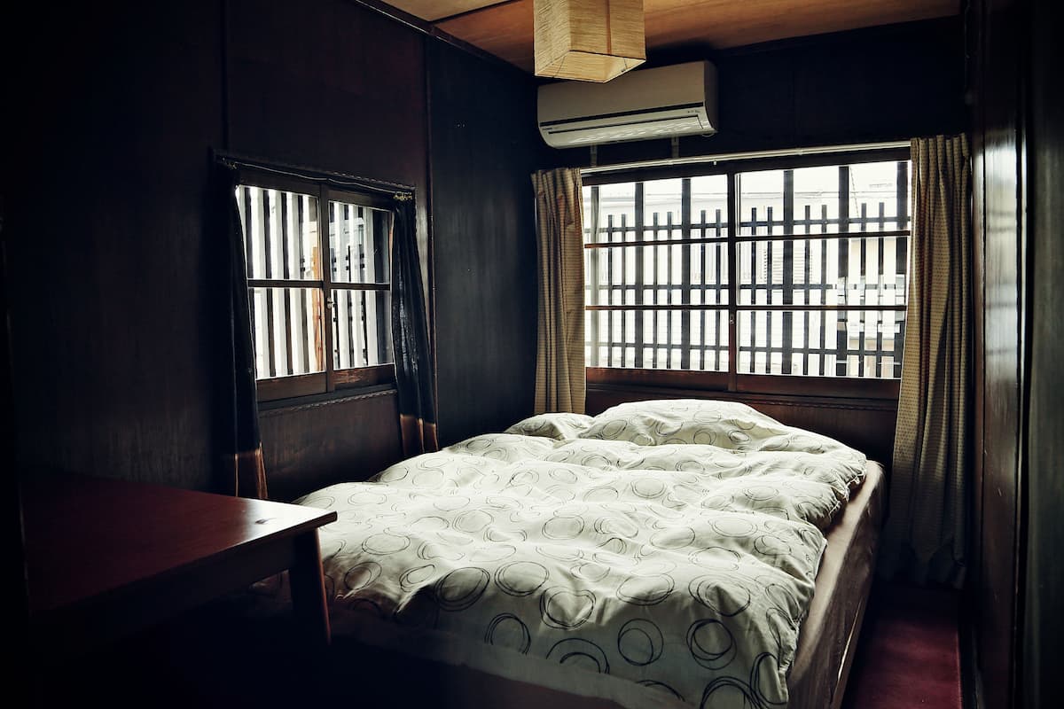 A bedroom with a bed, a wooden desk, and a window with barred glass.
