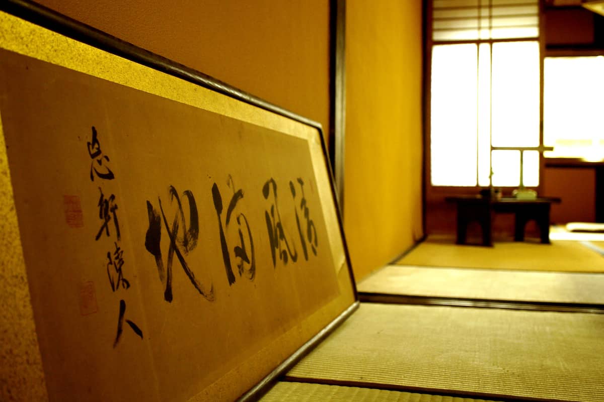 A traditional Japanese room with tatami flooring, a shoji screen, and calligraphy on the wall.