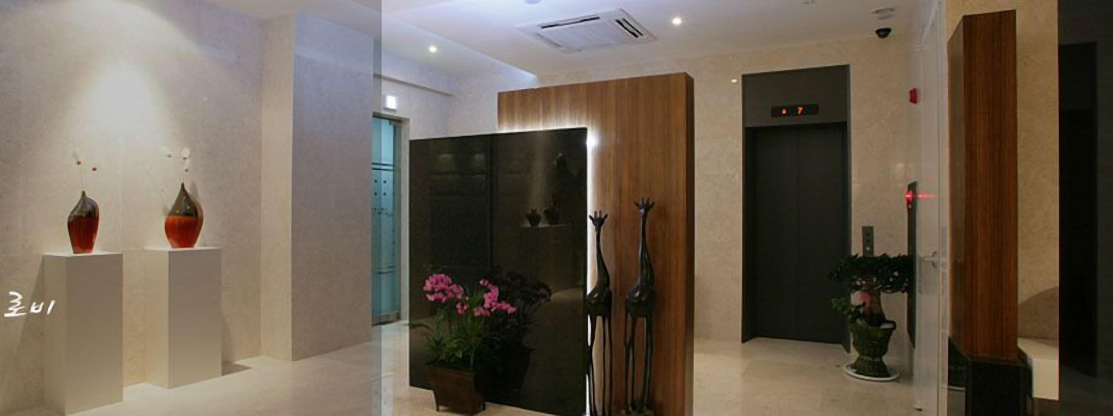 A modern lobby with a reception desk, a wooden panel wall, and a digital elevator display.
