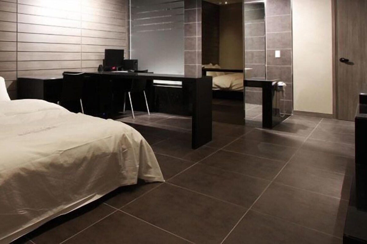 A modern hotel room with a large bed, a desk, and a separate sleeping area.