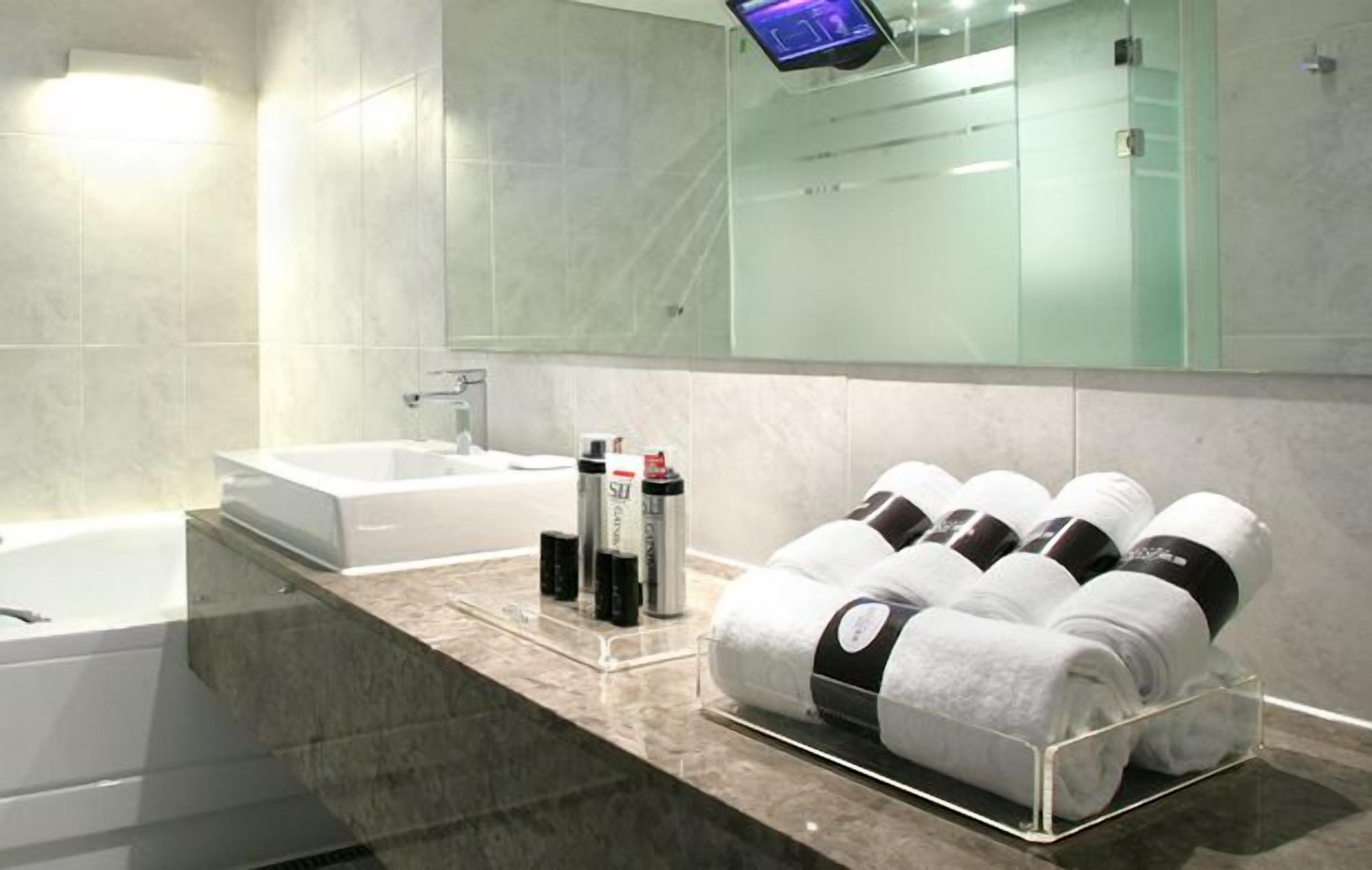 A modern bathroom with a large mirror, a bathtub, and a towel rack with neatly rolled towels.