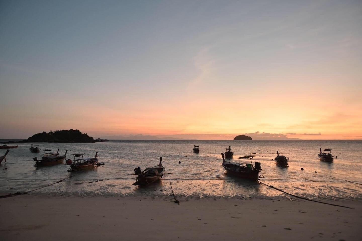 Una playa con barcos anclados en el agua y una isla distante.