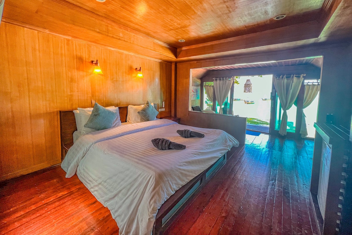Un dormitorio con paneles de madera, una cama grande, dos luces fijadas a la pared y un ventanal con cortinas.
