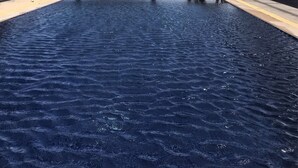 Une piscine rectangulaire dotée d’une terrasse en bois et de chaises longues, offrant une vue sur une mer d’un bleu limpide et sur des îles lointaines.