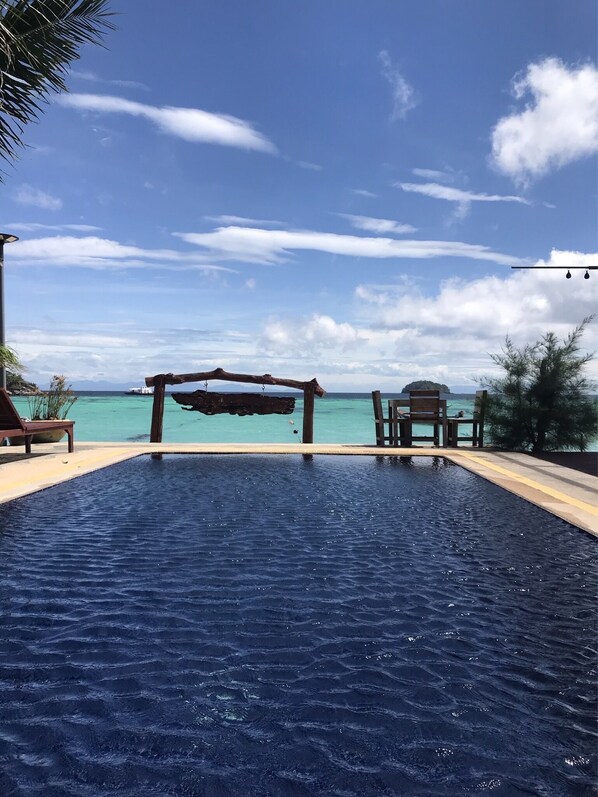 A rectangular swimming pool with a wooden deck and lounge chairs, overlooking a clear blue sea and distant islands. - Lipe Power Beach Resort (Koh Lipe)