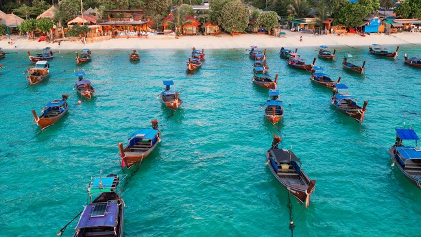 Une plage où de nombreux bateaux sont amarrés dans une eau turquoise et cristalline.