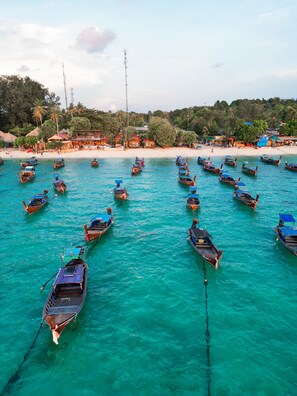 A beach with numerous boats anchored in clear turquoise water. - Lipe Power Beach Resort (Koh Lipe)