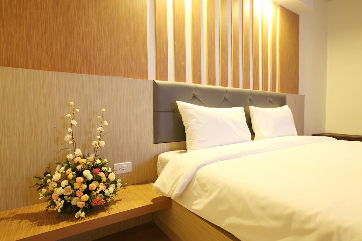 A hotel room with a bed, a wooden nightstand, and a wall-mounted light fixture.