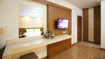 A hotel room with a bed, a TV mounted on the wall, a wooden desk, and a mirror.