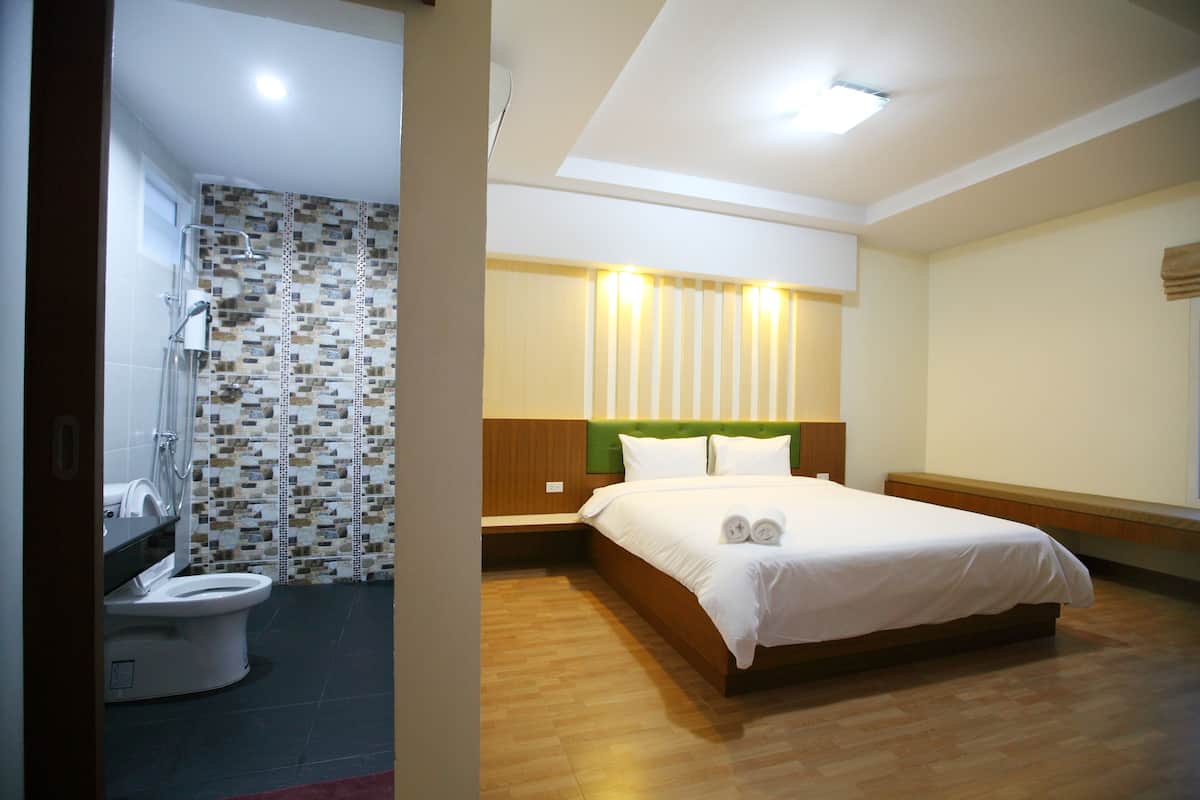 A hotel room with a shower, toilet, bed, and bedside table.